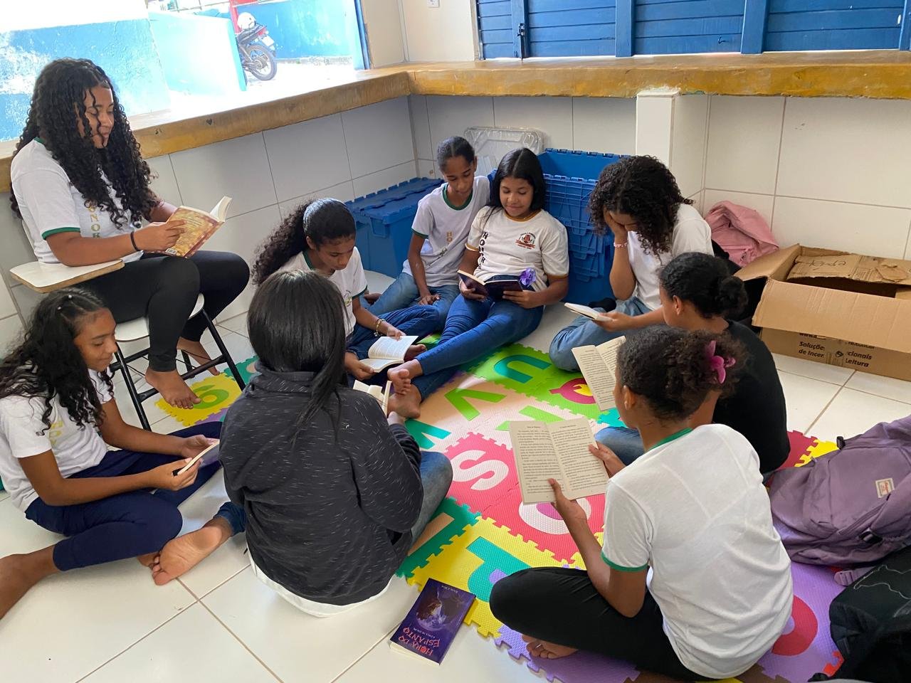 Roda de leitura com estudantes sentados no tapete alfabético